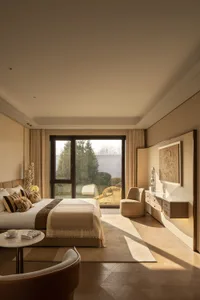 A modern bedroom with a wooden floor, a bed, a chair, and a table, lit by natural light from a window