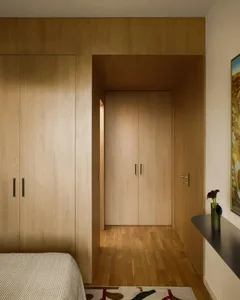 A cozy bedroom with wooden floors and door, featuring a bed, dresser, and painting on the wall, with a warm and natural ambiance