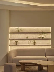 Cozy living space with beige walls, a couch, coffee table, and shelf, well-lit for a comfortable atmosphere