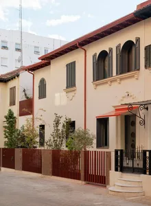 一棟白色外牆、紅色屋頂的住宅建築物，擁有木製紅色圍欄，二樓陽台，兩個花盆