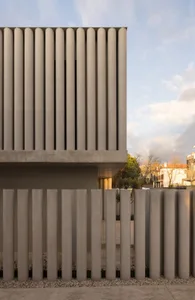 Photograph of a modern building with a concrete wall and vertical concrete panels, well-lit from unknown sources