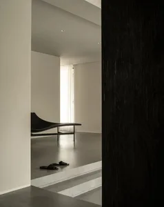 A dimly lit room with a black couch and bench in a minimalist and modern space with a black and white color scheme
