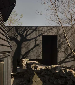 A modern house with a wooden exterior, large window, and door, surrounded by trees, in a calm and serene natural setting