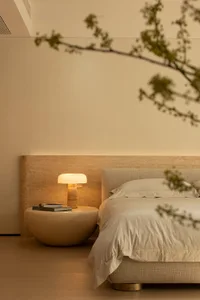 A cozy bedroom with a wooden bed, a table lamp, and a book, featuring soft and warm lighting and inviting atmosphere