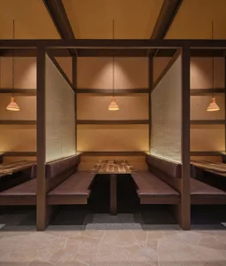 A modern restaurant with a wooden interior, featuring a dining area with tables and benches, a bar with a counter, and dim lighting creating a cozy ambiance
