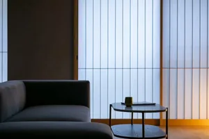 Cozy modern living room with a gray couch, a black table, and dim lighting, decorated with a cup and a vase, featuring wood and metal materials