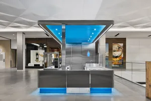 A modern kitchen with a large island, stainless steel countertops, and a sleek contemporary design, featuring a refrigerator and sink, with bright lighting and neutral colors