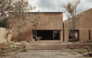 A modern outdoor dining space with a brown house, a dining table, a couch, and a sink, set against a natural background with a tree and sunlight streaming in through the windows