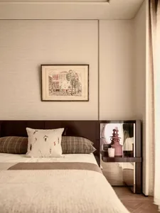 Cozy bedroom with a bed covered in a white blanket, a wooden headboard, and a picture frame on the wall, with a table and lamp nearby