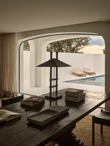 A modern living room with a pool in the background, featuring a dining table, two couches, and various books, creating a cozy and inviting atmosphere