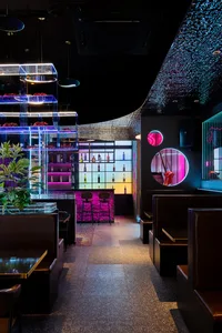 Modern bar and restaurant interior with black and white decor, featuring multiple chairs, dining tables, and a well-stocked bar with bottles and wine glasses