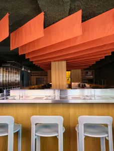 Cozy restaurant interior with a dimly lit bar area featuring a wooden counter and white chairs, surrounded by bottles, cups, and bowls