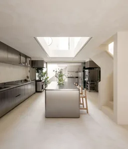 Modern kitchen and dining space with a large island, dining table, potted plants, and vases, featuring a clean and functional design