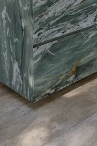 A modern kitchen countertop made of marble with a wooden drawer, lit by natural sunlight