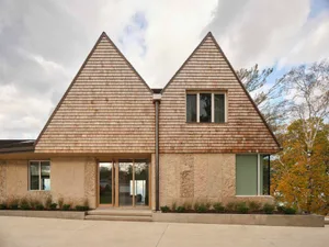 A warm and inviting beach house with a triangular shape, featuring a combination of stone and wood materials, and numerous windows for natural light