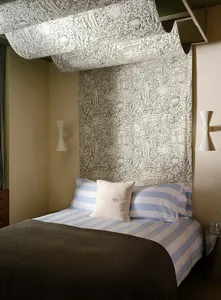 Cozy bedroom with a bed, a pillow, and a patterned wallpaper featuring people, in a dimly lit space with a simple and clean design