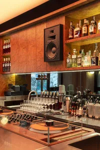A dimly-lit bar with wooden shelves and counter, stocked with a variety of liquor bottles and glasses