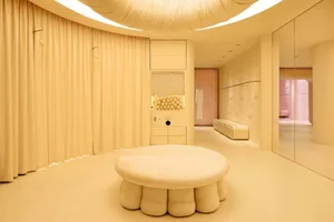 A modern living space with a white color scheme, featuring a round table, bench, sink, and dining area with chairs, adorned with pictures and a vase