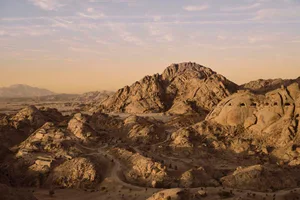 A serene and dramatic mountainous landscape with brown rocky terrain and a vast desert environment under natural sunlight