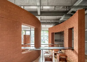 Cozy dining space with a brick wall, a large dining table, and potted plants, surrounded by modern furniture and kitchen area