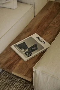 A modern hotel lobby with a white couch on a wooden floor, a magazine on top, and a sleek building in the background