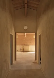 A dimly lit hallway with a doorway and a light fixture, featuring concrete walls and a mysterious atmosphere