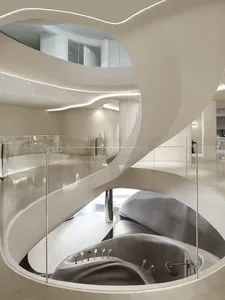 A spiral staircase made of white marble is surrounded by glass walls, allowing natural light to fill the space and creating a bright and airy atmosphere