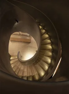 A modern spiral staircase in a room with a wooden floor and a window in the background, surrounded by a modern architectural design