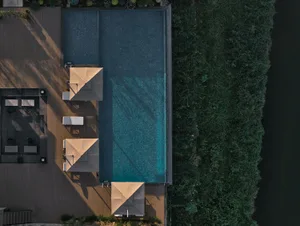 A well-maintained pool area with a blue pool surrounded by umbrellas in a backyard setting