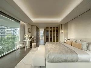 A well-lit modern bedroom with a white bed, gray pillow, and minimalistic decor, featuring a chair and couch in a comfortable and inviting space