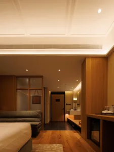 Cozy hotel room with a wooden floor, brown color scheme, a bed near the left side, a couch on the right, and a bathroom in the back with a sink and mirror