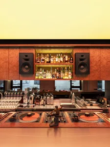 A dimly lit modern bar with a wooden countertop, displaying a variety of liquor bottles and glasses, creating a cozy and inviting atmosphere