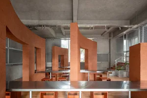 A modern restaurant with a large dining table and benches, surrounded by concrete walls and wooden accents, in a well-lit space