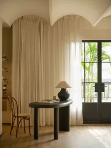 A modern room with a white curtain, black table, and two chairs, well-lit by natural light from a window