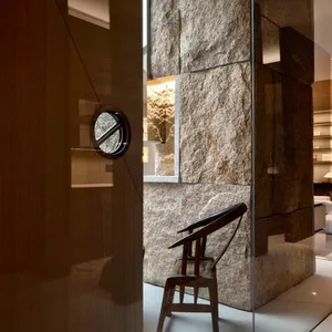 Cozy living area with a wooden door, rock wall, chair, and dining table, lit by natural light from a window