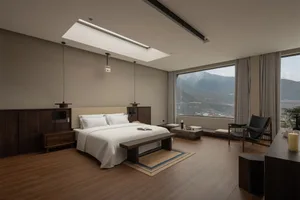 Cozy bedroom with a wooden floor, a bed near a window with a view of the mountains, and a chair, lit by natural light