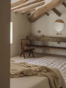 Cozy bedroom with a wooden bed, chair, and sink, featuring a white blanket and wooden walls