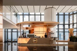 A cozy coffee shop with a wooden counter, cups, and bottles, and a person serving customers