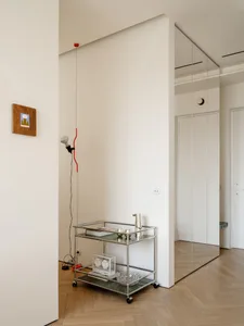 A calm and inviting living space with a white wall, metal shelf, glass clock, and red wire, lit by natural sunlight