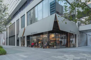 A modern building with a large glass window and gray awning, surrounded by natural light and inviting atmosphere