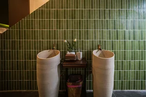 Bathroom with two white sinks, a green accent wall, a vase with flowers, and dim lighting