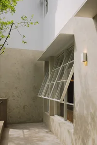 A stone building with an open window and closed door, set in a serene courtyard with a tree in the background