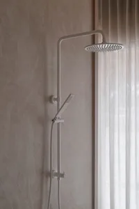 Bathroom with a white shower head on a concrete wall, natural light from a window, and a minimalist aesthetic