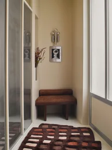 Bathroom with a brown bench, rug, and mirror, featuring a warm and inviting atmosphere with natural lighting