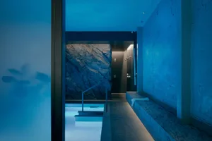 blue-toned bathroom with a large pool, bench, and shower, featuring a modern and luxurious design with marble or high-end tiles