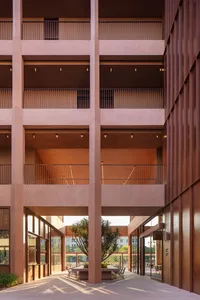 A large, empty building with a red brick exterior, a large atrium, and a balcony on the upper level, bathed in natural light
