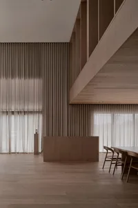 Well-lit living room with wooden floor, walls, and dining table, featuring natural light and a warm atmosphere