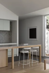 Modern kitchen with a white marble countertop, a window, a sink, a refrigerator, and a dining table with white chairs, lit by natural light