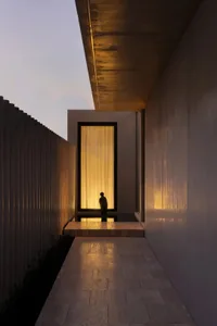 A person stands in front of a modern building with a glass and concrete facade, surrounded by a calm and serene atmosphere