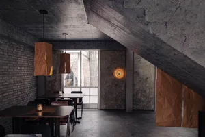 Cozy restaurant with a modern design, featuring a dining area, bar, wood, and concrete elements, with dim lighting and natural light from windows